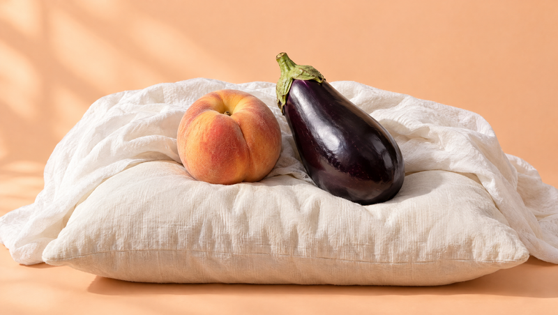A peach and an eggplant relaxing side by side on a soft cream pillow
